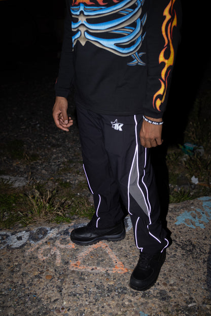 Person wearing a black hoodie with colorful designs and black pants with white stripes on a dark background.